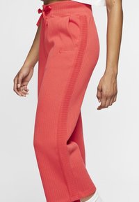 Korallfärgade ribbade sweatpants med dragsko i midjan, sidofickor och Nike-logotyp på vänster höft. Mjukt tyg med texturerad design.