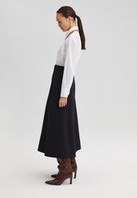 Black midi skirt with a smooth texture, paired with a white button-up shirt. Notable metallic hardware accents and brown heeled boots.