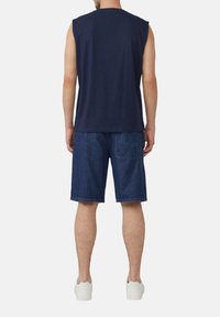 Navy-blaues ärmelloses Shirt kombiniert mit Denim-Shorts; die Shorts besitzen eine Gesäßtasche und einen lockeren Schnitt; das Modell trägt weiße Sneakers.