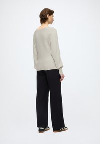 Svetlobéžový rebrovaný sveter s klesajúcimi ramenami, kombinovaný s čiernymi širokými nohavicami a čiernymi teniskami s bielymi pruhmi.