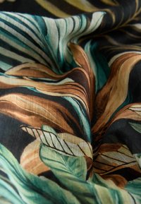 Material cu un model de frunze tropicale în nuanțe de verde, maro, bej și negru, prezentat în prim-plan cu pliuri și textură vizibile.