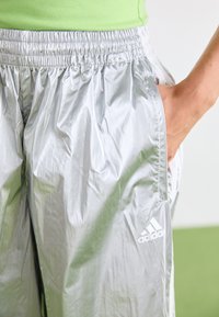 Pantalons de sport argentés en matériau léger et brillant. Présentent une taille élastique et des poches latérales. Logo Adidas affiché en évidence.