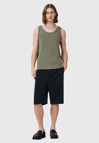 Olivgrünes Tanktop kombiniert mit schwarzen Shorts, mit lockerer Passform und glattem Stoff. Auffälliges Detail: Silberne Kettenhalskette.