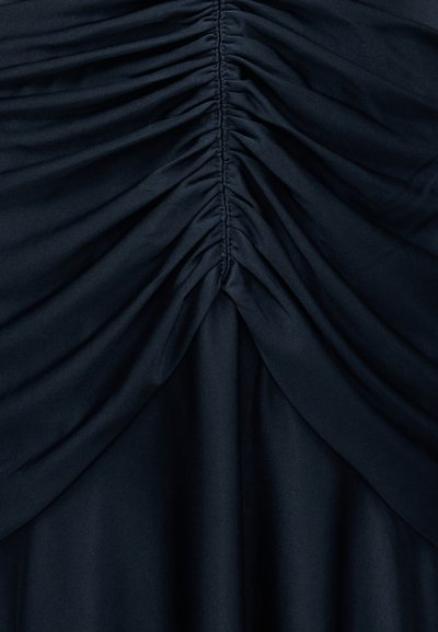 Σκούρο ύφασμα με στενό ραφινάρισμα στο κέντρο που δημιουργεί δομημένες κάθετες πτυχώσεις και μια συγκεντρωμένη, ντυμένη υφή.