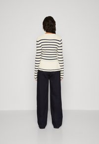 Pull rayé crème et marine à manches longues avec un ourlet en peplum, associé à un pantalon en denim foncé ample ; texture lisse.