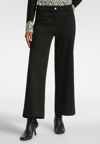 Pantalones de pierna ancha negros de denim con un acabado limpio, que presentan bolsillos laterales y se combinan con botas negras hasta el tobillo.