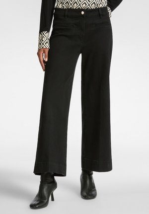 Pantalones de pierna ancha negros de denim con un acabado limpio, que presentan bolsillos laterales y se combinan con botas negras hasta el tobillo.