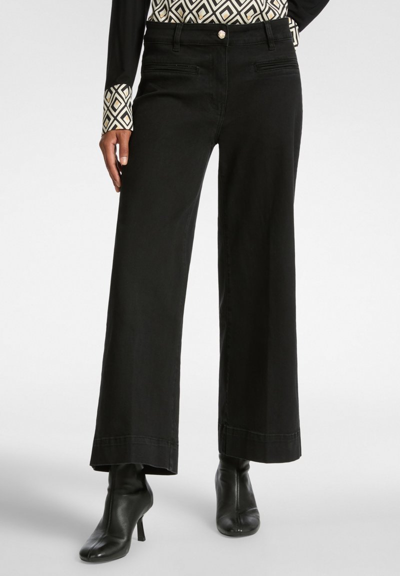 Pantalones de pierna ancha negros de denim con un acabado limpio, que presentan bolsillos laterales y se combinan con botas negras hasta el tobillo.