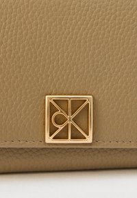 Ταμπά δερμάτινο πορτοφόλι με ανάγλυφο γεωμετρικό λογότυπο από μέταλλο σε χρυσή απόχρωση με στιλιζαρισμένο σχέδιο και υφή με ελαφριά γυαλάδα.