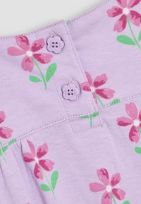 Tela de lila con un patrón de flores rosas. Presenta dos botones morados en forma de flor en la parte posterior y un diseño plisado en la cintura.