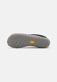 Schwarze Schuhsohle mit einem strukturierten grauen Muster, versehen mit einem gelben Markenlogo und geometrischen Traktionselementen für Grip und Stabilität.