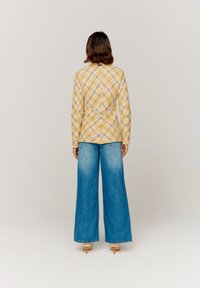 Blazer giallo a quadri con un design slim fit, abbinato a jeans a gamba larga blu chiaro con effetto sbiadito, che mostrano una silhouette rilassata.