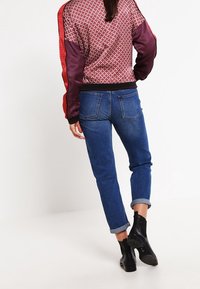 Red and purple patterned bomber jacket with black cuffs, paired with rolled-up blue denim jeans and black ankle boots.