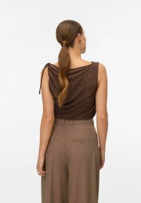 Rudas drapiruotas viršus su metaliniais siūlais, plonais petnešėlėmis ir minkšta tekstūra, derinamas su aukštu liemeniu, smėlio spalvos pritaikytomis kelnėmis.