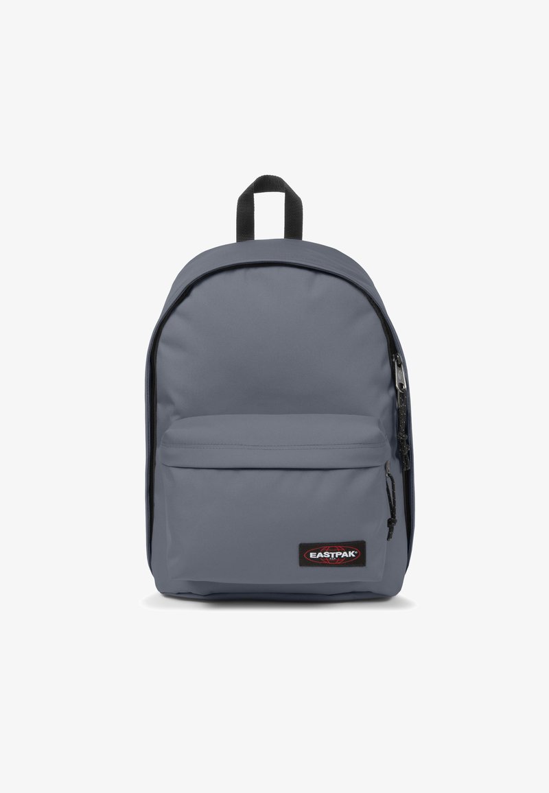 Mochila gris hecha de tela duradera, que cuenta con un amplio compartimento principal, un bolsillo frontal con cremallera y un asa en la parte superior para llevar. Presenta detalles en negro.