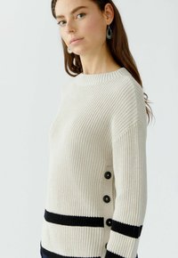 Strickpullover in Creme mit schwarzen horizontalen Streifen. Verfügt über einen Rundhalsausschnitt und einen Knopfdetails entlang der Seite, mit einer strukturierten Webart.