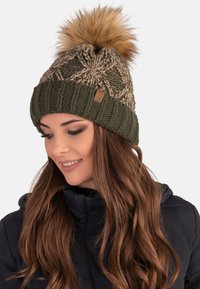 Beanie lavorato a maglia color khaki con un motivo testurizzato e un grande pompon in pelliccia sintetica sulla parte superiore. Presenta una targhetta in pelle marrone sul polsino.