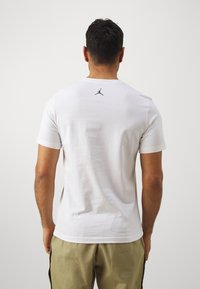 Fehér pamut póló rövid ujjal, középen fekete Jordan logóval a felső háton. Simaság jellemzi, klasszikus kerek nyakú fazon.