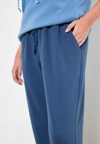 Niebieska bluza z regulowanym kapturem, połączona z ciemnoniebieskimi dresami, które mają boczną kieszeń i miękką, gładką fakturę tkaniny.