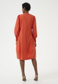 Orange puffärmad klänning i lätt material, knälång med rak silhuett. Har rund halsringning och samlade detaljer.