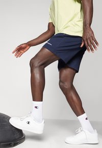 Navy shorts with white logo, paired with white sneakers and socks featuring a small logo. Individual in motion, highlighted by muscular legs.