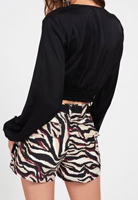 Haut noir à manches longues avec une taille smockée, associé à un short imprimé zèbre multicolore offrant une coupe décontractée et des poches latérales.