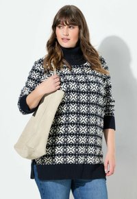 Sweter dziany w granatowo-białym wzorze geometrycznym, z kołnierzem typu golf i ściągaczami na mankietach. Trzymany z dużą beżową torbą.