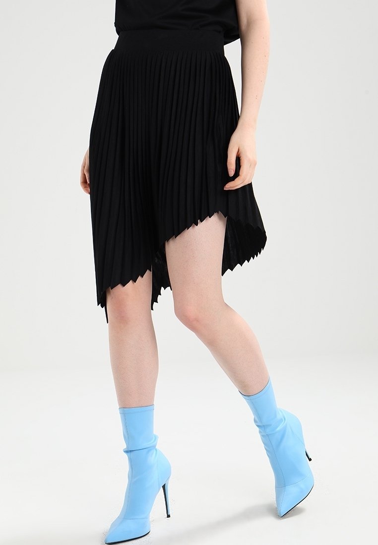 Falda plisada negra con un dobladillo asimétrico, hecha de un tejido ligero. Combinada con botas de tacón azul, que destacan por su textura suave y diseño ajustado.