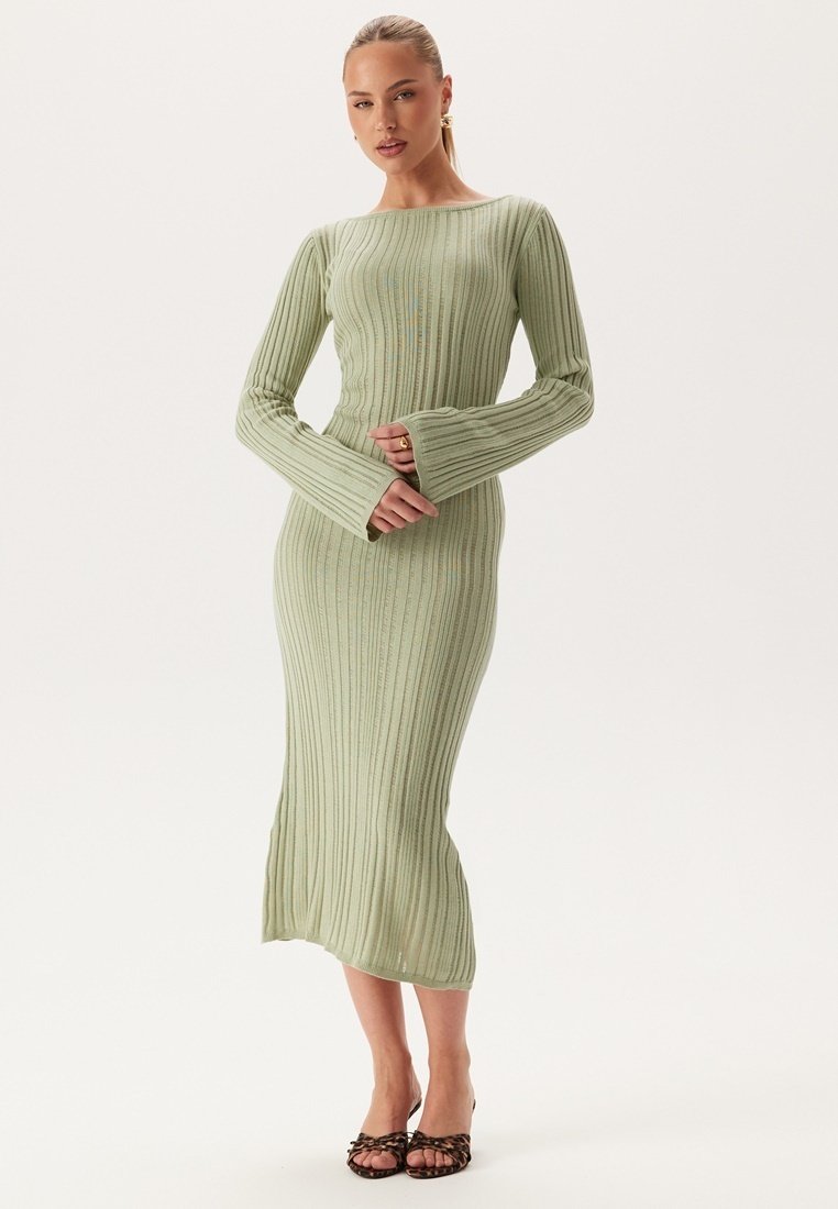 Robe à manches longues côtelée en vert clair, avec une coupe ajustée et des manches évasées, atteignant le mollet, associée à des sandales à bout ouvert.