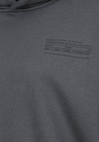 Grijze sweatshirt met een zachte textuur, voorzien van zwarte bedrukte tekst die thema's van geluk en zelfzorg benadrukt.