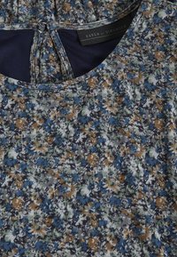 Blusa floral con fondo azul marino, con un patrón floral multicolor en azul, verde y marrón. Cuello redondeado y cierre con botones.