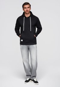 Černá mikina s kapsou na klokaním břiše, bílými šnůrkami a malou nášivkou s logem. V kombinaci se světle šedými džíny a černými teniskami.