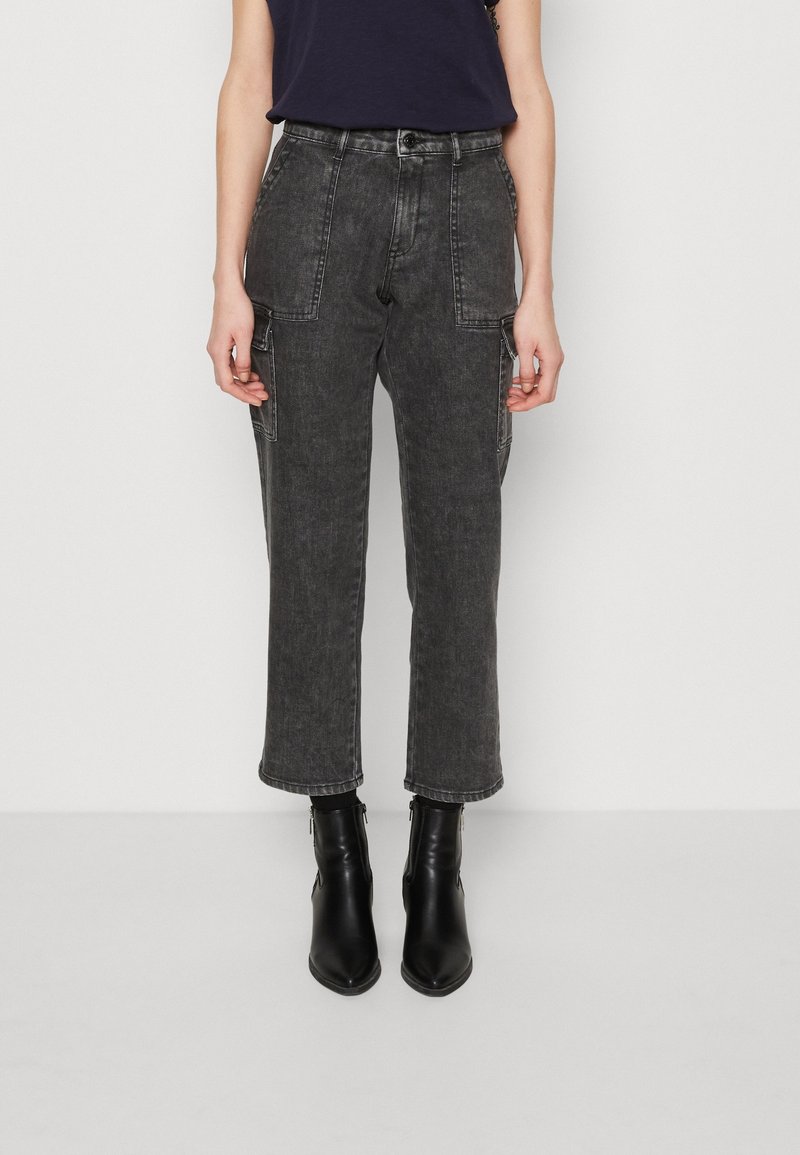 Schwarze Denim-Cargohosen mit frontalen Taschen, geradem Schnitt, mittelhohem Bund, subtiler Textur und Umschlagsaum. Kombiniert mit schwarzen Stiefeletten.