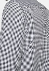 Camisa de cuadros en blanco y negro con un diseño ajustado, que cuenta con un cuello impecable y una tela texturizada, mostrando un patrón de gingham a pequeña escala.