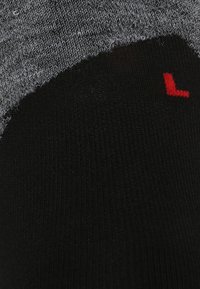 Chaussette grise et noire avec une texture côtelée ; présente une étiquette rouge "L" sur la partie noire, indiquant la désignation pour le pied gauche.