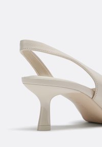 Bež usnjena čevlja z naramnico, s koničasto sprednjo in zmerno blok peto. Teksturirana površina z gladkim zaključkom na peti.