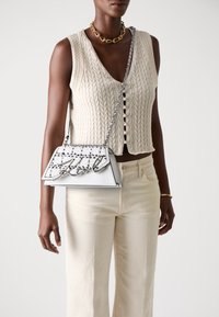 White structured handbag featuring a quilted texture, silver chain strap, and a bold "Girl" logo accent. Worn with a beige knitted top.