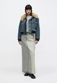 Džinsa jaka ar mākslīgās kažokādas apkakli, īss dizains, kombinēts ar garu divtoņu džinsa svārku. Melni kurpes ar mežģīnēm papildina tērpu.