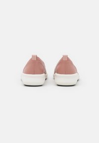 Scarpe slip-on in pelle rosa con una texture liscia, suole in gomma bianca e piccoli tasselli sul retro. Design minimalista e silhouette semplice.