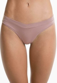 Vrouw in licht mauve naadloze bikini-achtige onderbroek met een crisscross tailleband, getoond van taille tot bovenbenen.