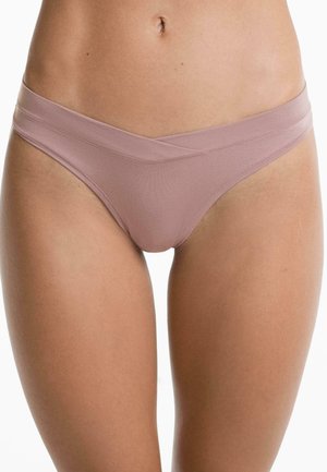 Vrouw in licht mauve naadloze bikini-achtige onderbroek met een crisscross tailleband, getoond van taille tot bovenbenen.