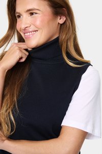 Mornarsko rebrasto pulover s turtleneckom, nad katerim je oblačen beli kratkoslečeni srajc, ki prikazuje gladko teksturo in sproščen dizajn.