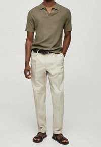 Oliwkowa, prążkowana koszulka polo, kremowe spodnie w kant, czarny pasek i czarne sandały. Gładka faktura oraz luźny krój.