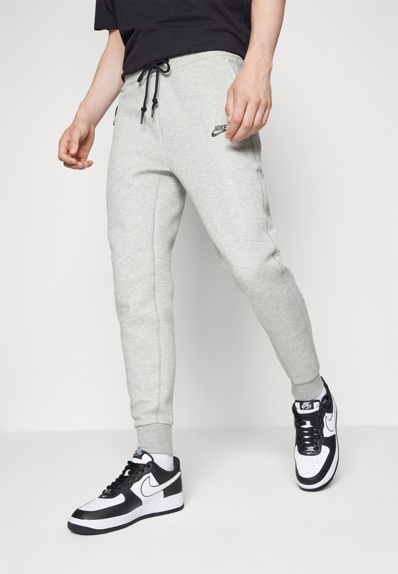 Hellgraue Jogginghose mit elastischem Bund und Kordelzug, ausgestattet mit Seitentaschen und gesteppten Details, kombiniert mit schwarz-weißen Sneakers.