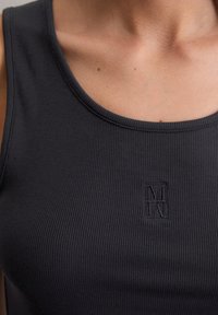 Zwarte geribde tanktop met een scoop neckline en een klein geborduurd logo in het midden. De stof lijkt zacht en aansluitend.
