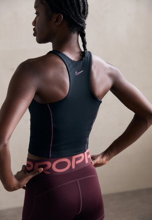 Zwarte sporttanktop met roze accenten, gecombineerd met bordeauxrode leggings met een opvallende logo-elastiek. Close-up van de achterkant.