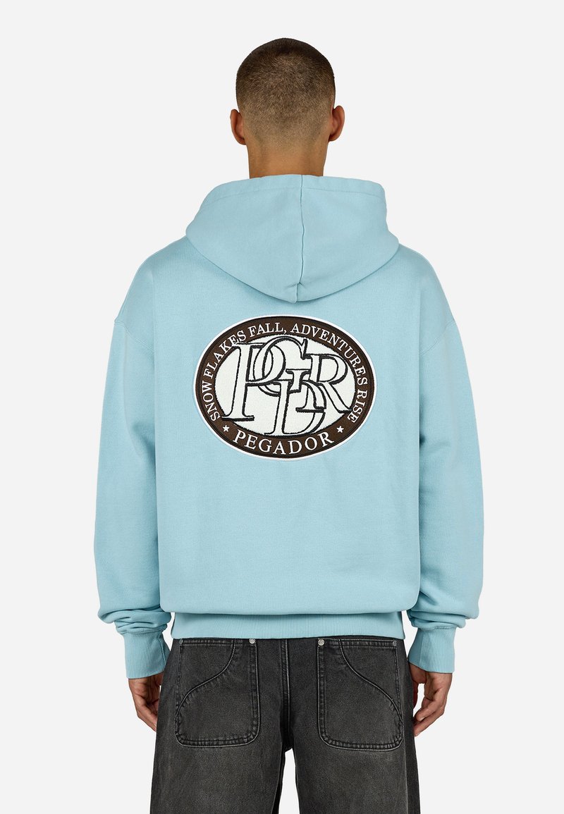 Γαλάζια Hoodie με μεγάλο κυκλικό καφέ κεντητό λογότυπο στο πίσω μέρος, το οποίο περιλαμβάνει κείμενο. Διαθέτει ευρύχωρη κουκούλα και πλισέ μανσέτες.