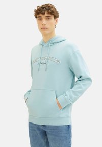 Sudadera azul clara con un bolsillo delantero, capucha con cordón y el texto "DENIM TOM TAILOR" impreso en el pecho. Tejido suave, corte relajado.