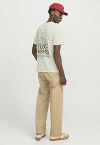 T-shirt di cotone verde chiaro con una stampa grafica sulla schiena, abbinata a pantaloni khaki e sneakers bianche con dettagli marroni.