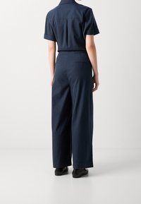 Ciemnogranatowy kombinezon z krótkimi rękawami, szerokimi nogawkami i prostym tyłem. Cecha to dopasowana talia i subtelne detale kieszeni.